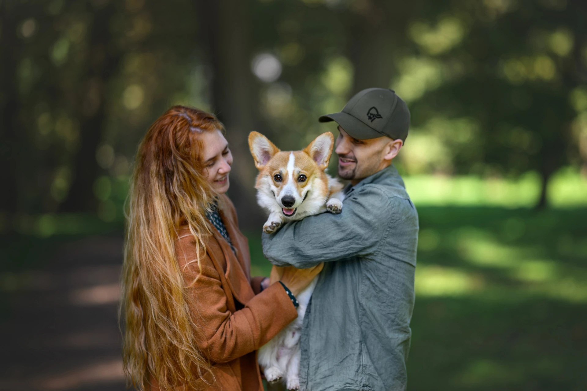 Pár s corgim v náručí v zeleném parku – společné focení s pejskem